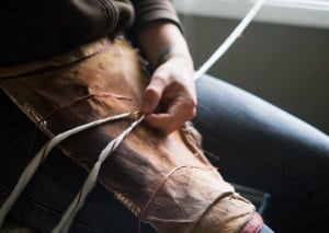 A man spins wool and cedar bark together on his lap