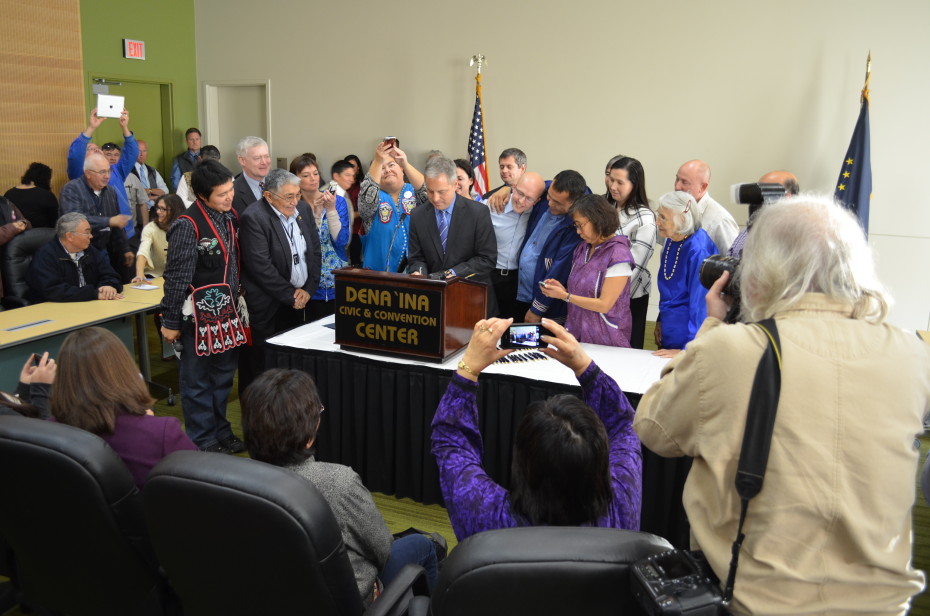 Gov. Sean Parnell signs HB 216 at the 2014 Alaska Federation of Natives Convention. The bill makes Alaska's Native languages official state languages. Looking on as the governor signs is Tlingit language teacher Lance Twitchell, Rep. Bennie Nageak, Rep. Charisse Millett, Lt. Gov. Mead Treadwell, First Alaskans Institute President Liz Medicine Crow, Sen. Lesil McGuire, Rep. Chris Tuck, Rep. Jonathan Kreiss-Tomkins, Rep. Doug Isaacson, Rep. Les Gara and others.