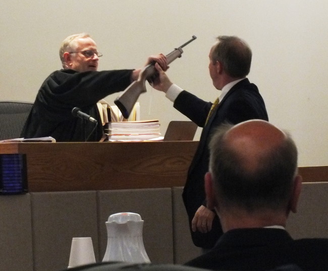 Attorney Mark Choate (right) hands over a 10-22 Ruger rifle that is similar to one used to shoot Simone Kim. Superior Court Judge Philip Pallenberg (left) wanted to inspect the firearm and make sure it was disabled before the jury entered the courtroom. (Photo by Matt Miller/KTOO)